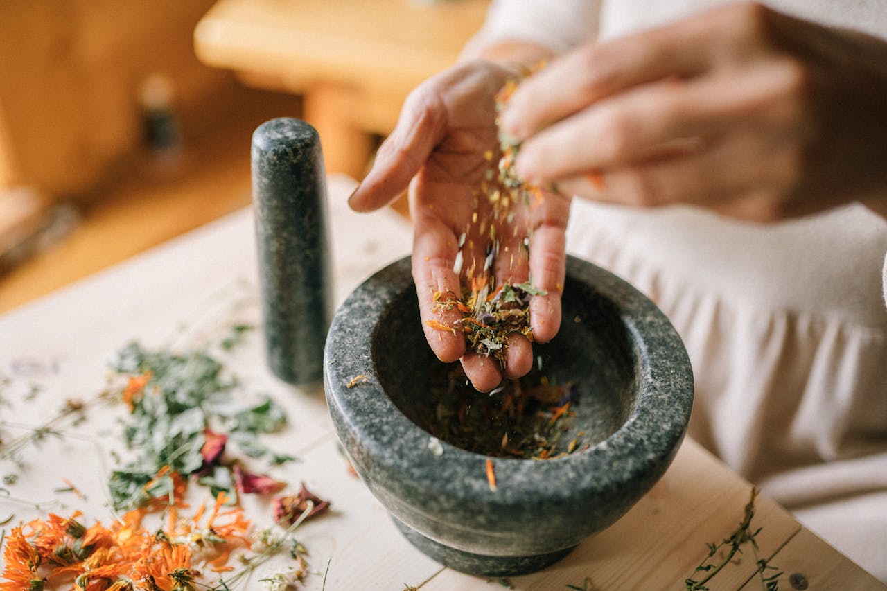 Close-up of herbs being prepared in a mortar and pestle by a woman, showcasing natural remedy techniques.